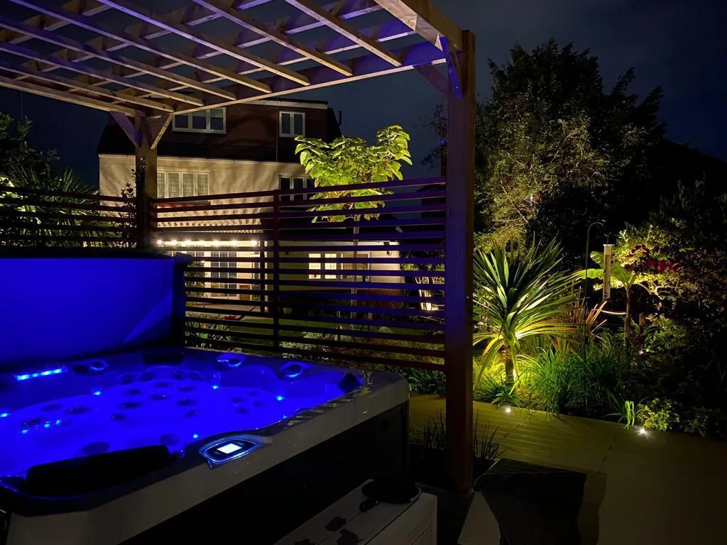 Hot tub lit in violet under a pergola with festoon lights and lush tropical planting